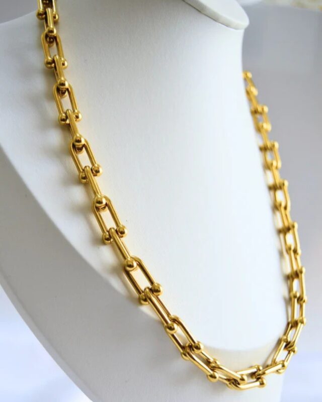 A close-up of an 18k gold pendant with a bold, premium design, reflecting soft golden light. The pendant rests on a neutral background, highlighting its luxurious shine and modern elegance.