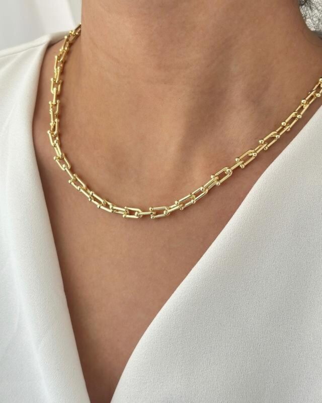 A close-up of an 18k gold pendant with a bold, premium design, reflecting soft golden light. The pendant rests on a neutral background, highlighting its luxurious shine and modern elegance.