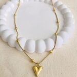 A gold pendant featuring a small heart enclosed within a bold circular frame, resting on a clean, neutral background. The piece gleams under soft light, highlighting its elegant balance of modern minimalism and romantic detail.