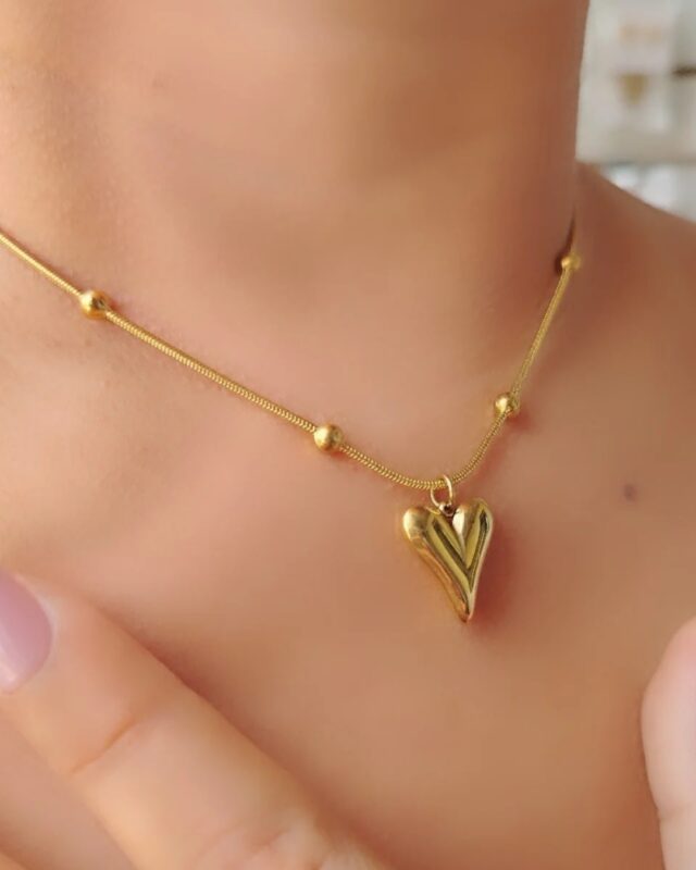 A gold pendant featuring a small heart enclosed within a bold circular frame, resting on a clean, neutral background. The piece gleams under soft light, highlighting its elegant balance of modern minimalism and romantic detail.